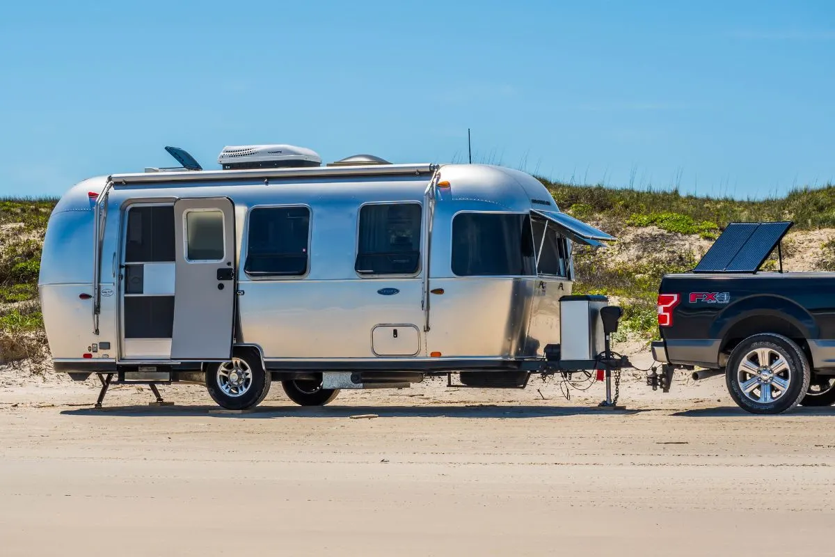 Side view of airstream travel trailer pulled by truck on road.