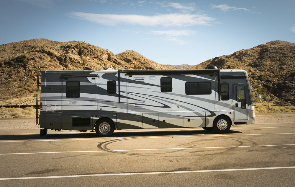 This is a gray and white class A motor home going through the desert road.