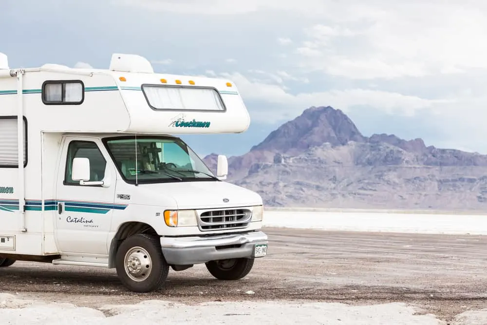 This is a white class C motor home traveling through the salt flats with views of mountains.