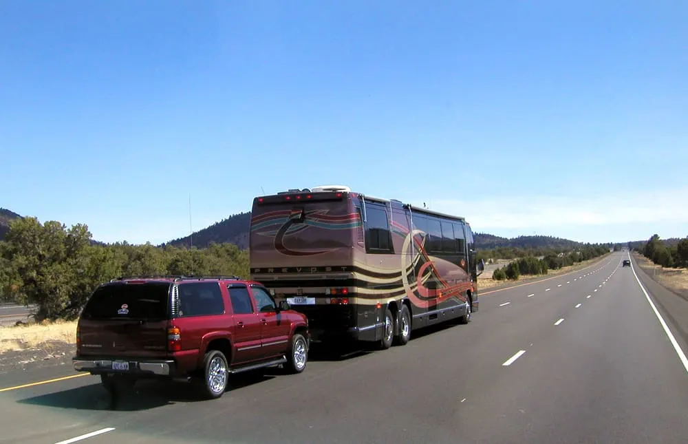 This is a black and gold class A motor home towing a truck behind.