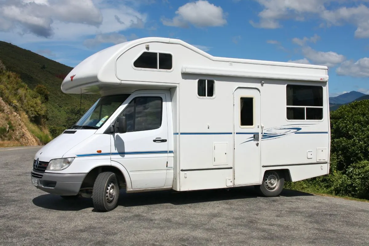 Side view of white Class B Campervan on mountain hill road.