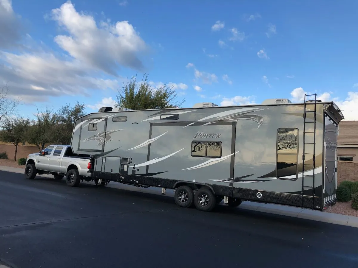 A Fifth wheel toy hauler towed by pick up truck on road.