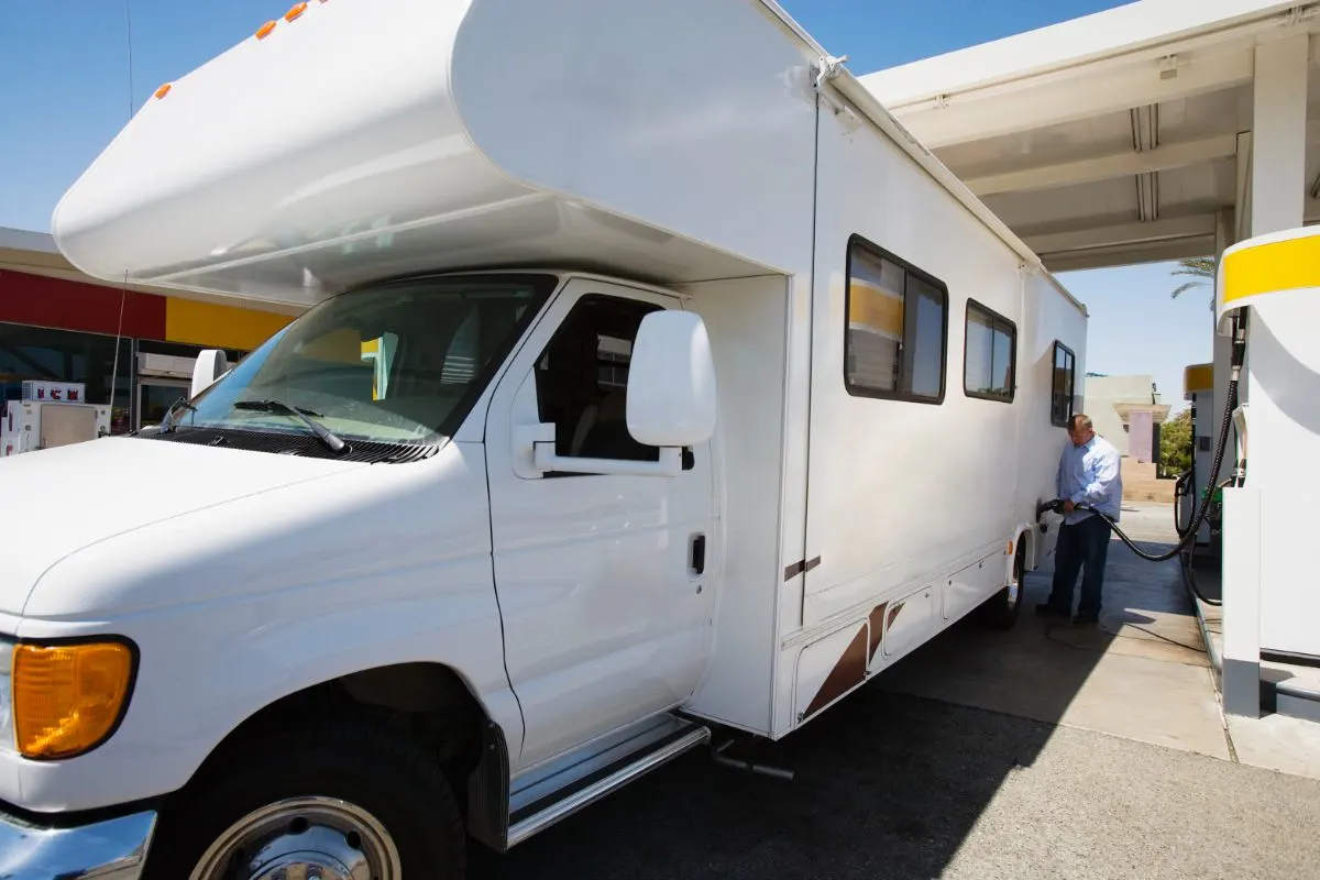 A photo of man refilling a fuel on the white rv in gas station.