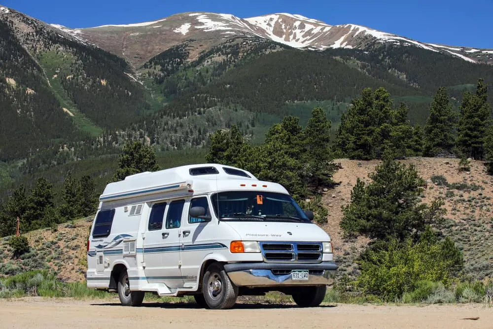 A motorhome parked on the side of the dirt road to a mountain camp site.