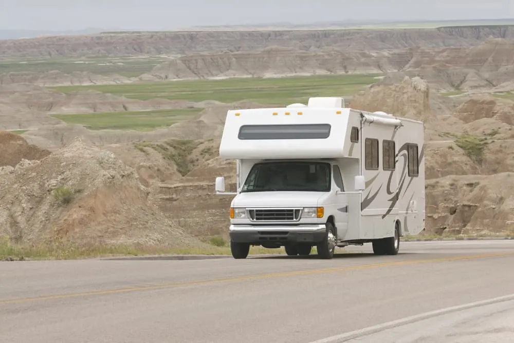 A white RV on a road to the mountains with a view of the hills below.