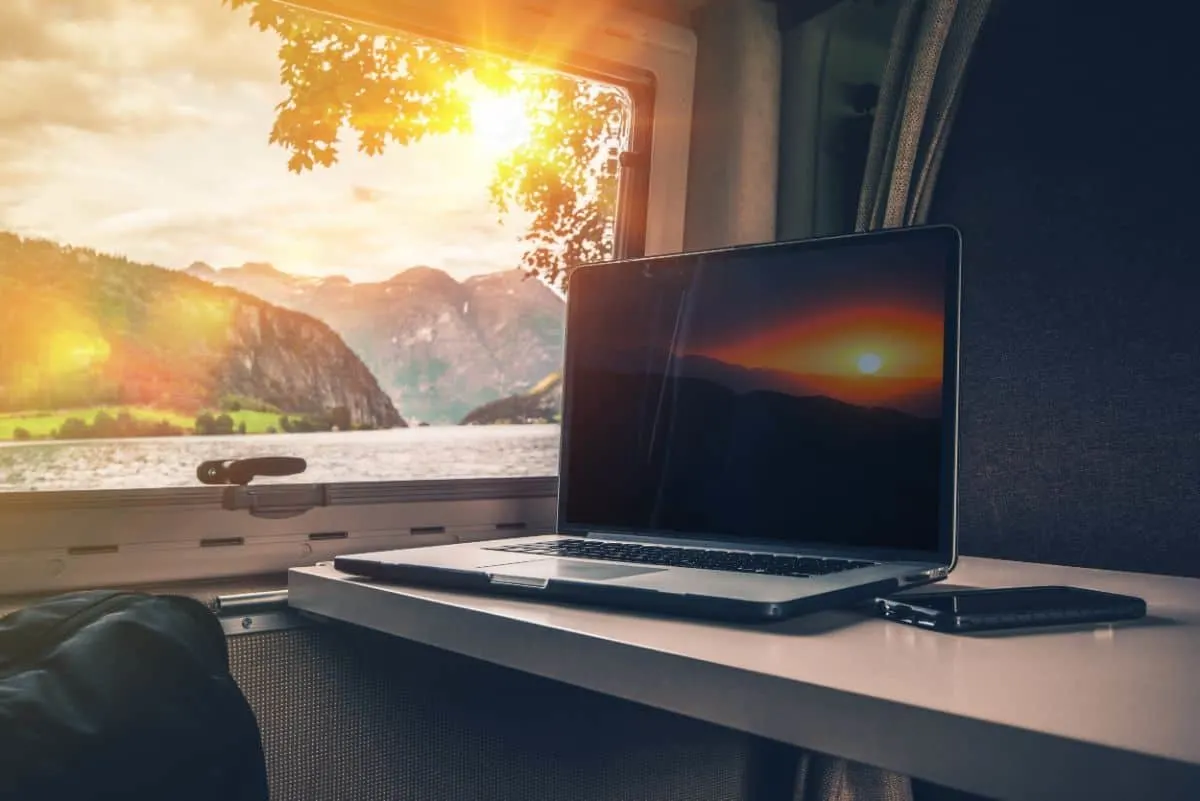 An open laptop and a smartphone on the table by the window inside an RV.