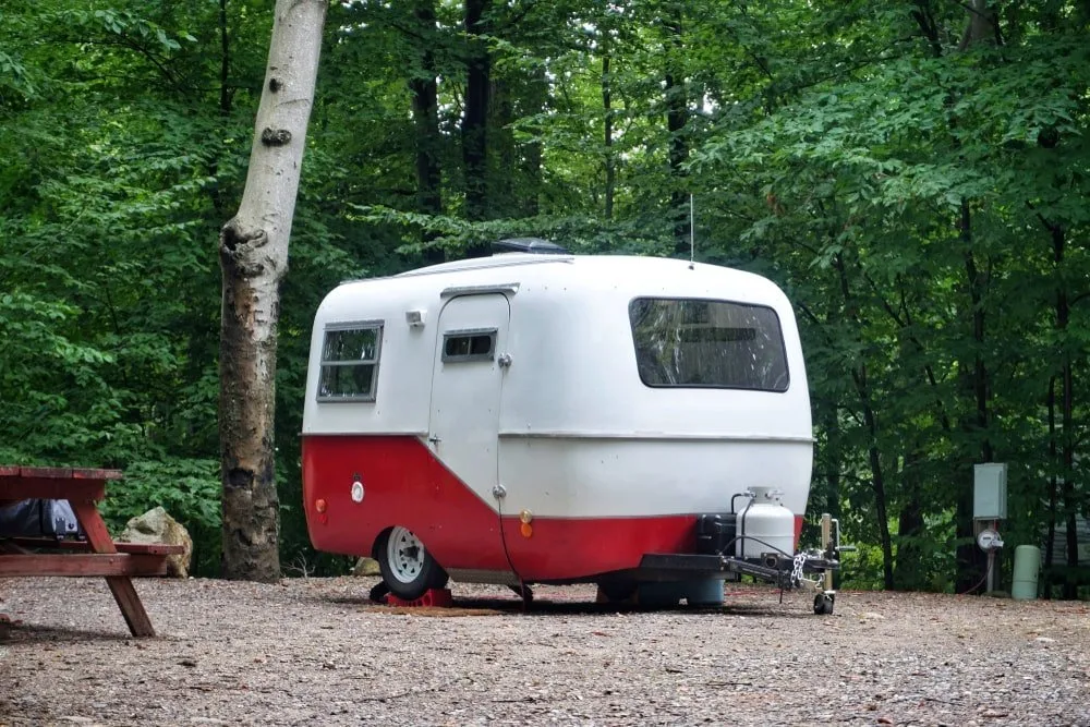 A red and white small camping trailer parked at a camping ground by the forest.