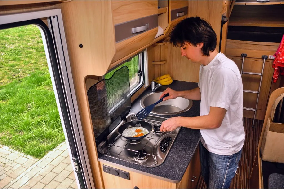 A man cooking breakfast in the kitchen of his RV during their family trip.