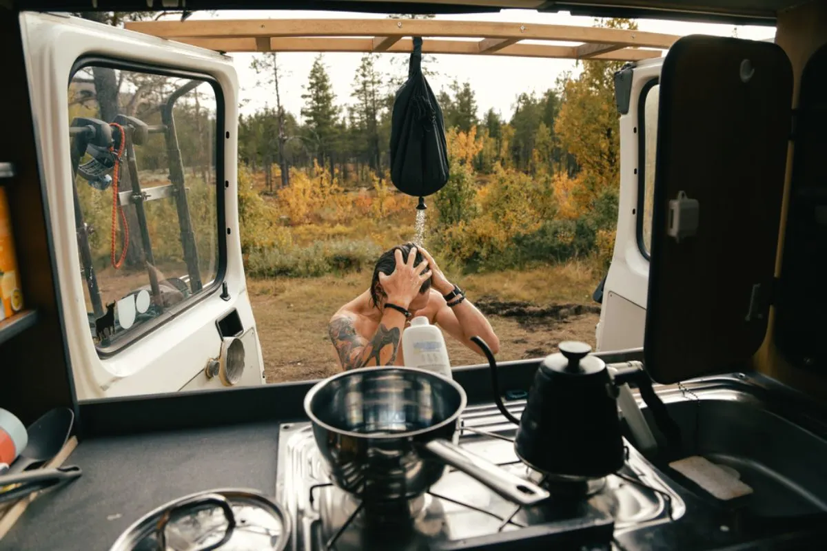 A man taking a bath outisde his RV using a shower while boiling some water.