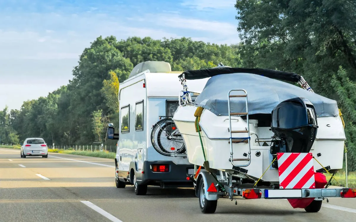 A RV on road towing a boat.