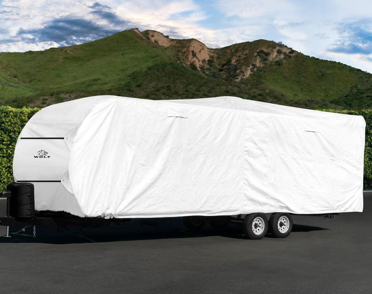 RV covered with an RV cover on the roadside near a hill.