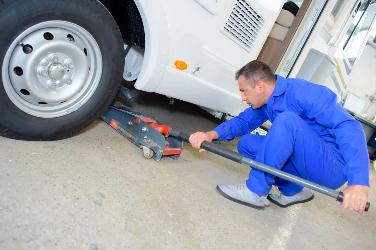 A mechanic man pushing jack under the vehicle.