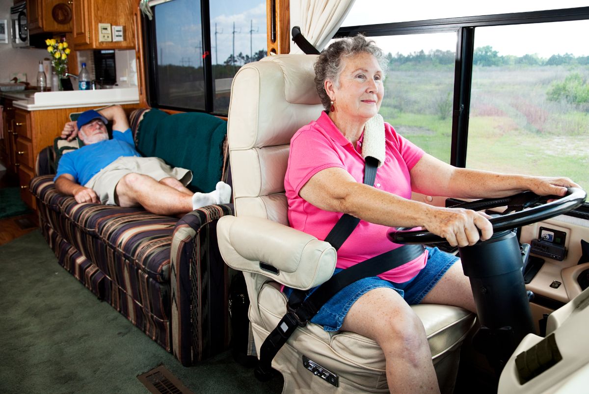 An old woman driving while her husband sleeping in the couch.