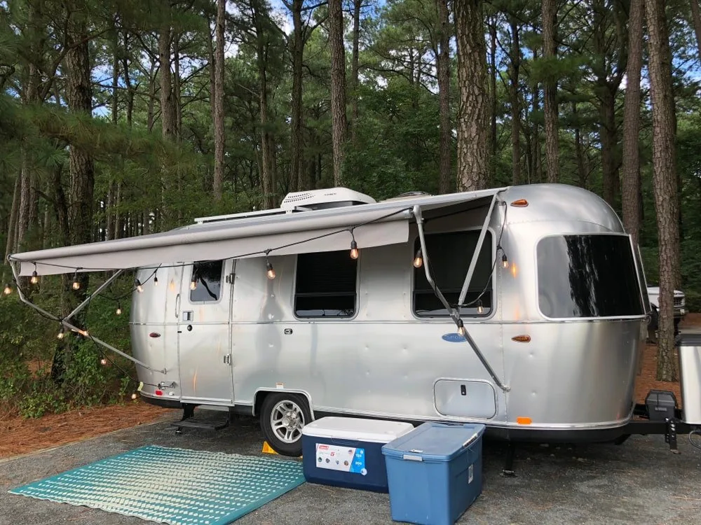 A silver stainless steel airstream travel trailer by a forest.