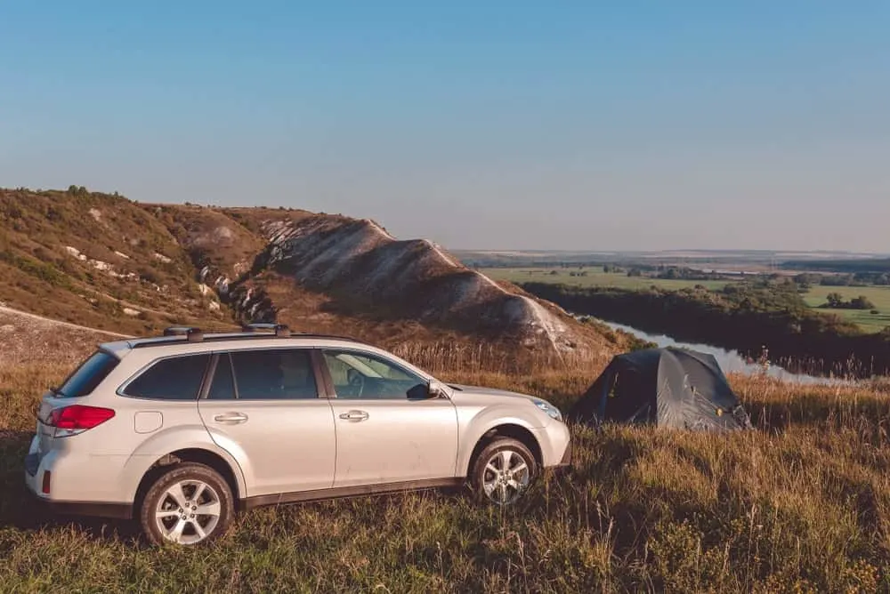 An SUV parked behind a pitched camp on a mountain top.