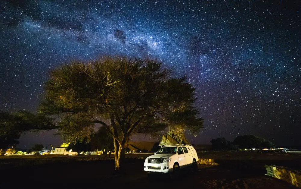 An SUV parked near a tree under breathtaking clear night sky views.