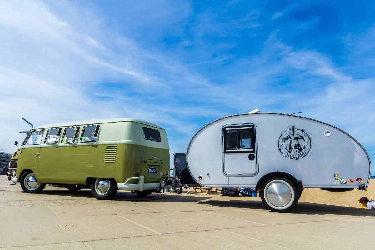 Side view of Teardrop Trailer pulled by classic Volkswagen van on road.