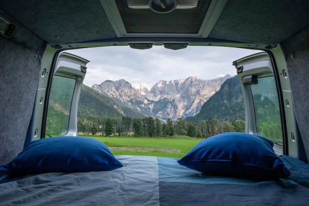 This is an interior look at a camper RV with a sleeping area that is open to the view of the mountains.