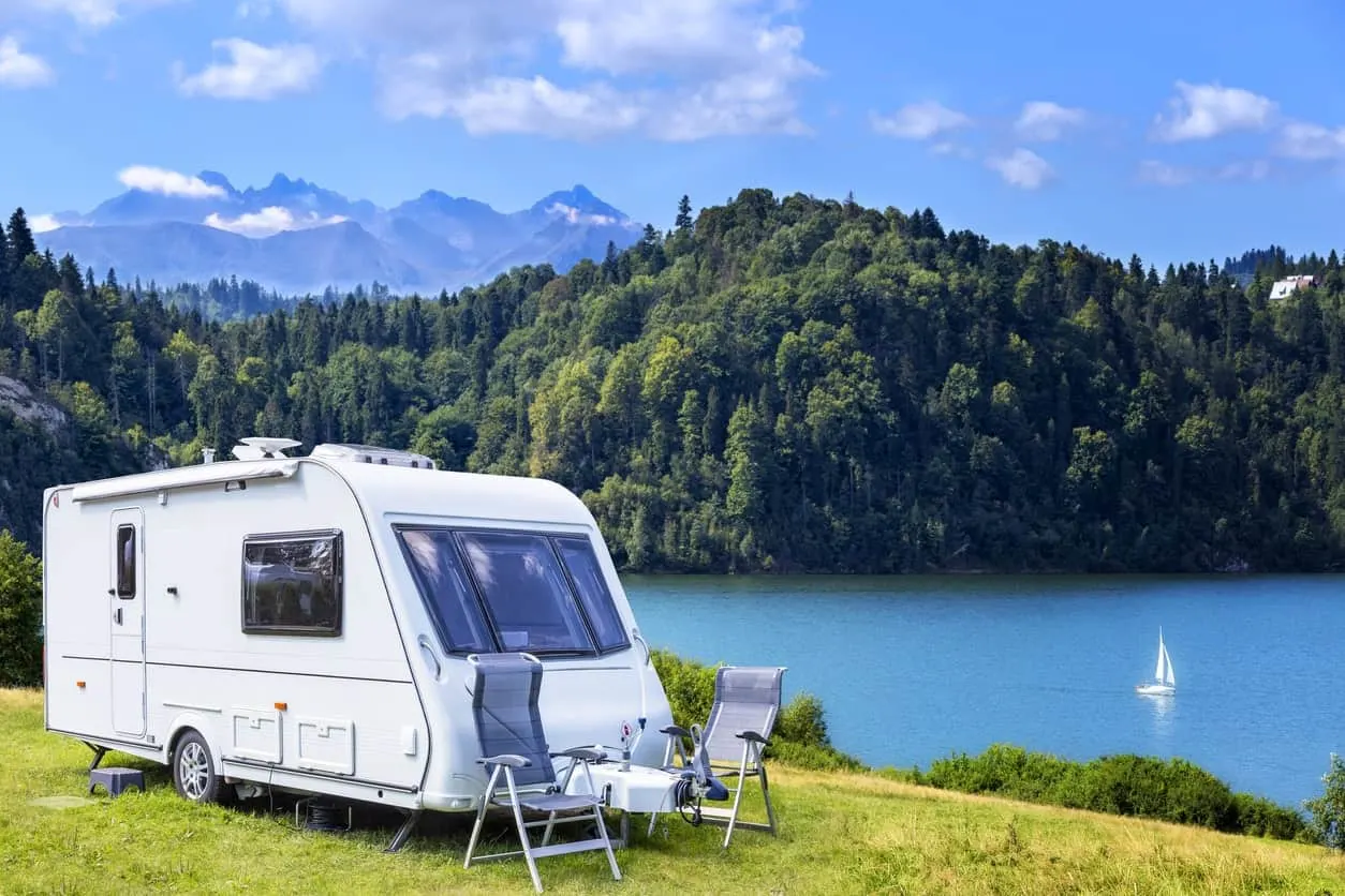 An RV is parked with outdoor table and chairs is parked with full view of the mountains and lake.