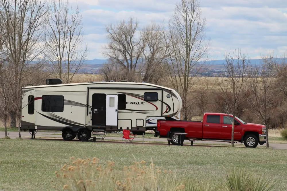 A fifth wheel RV and a red truck parked on the side of a camp site.