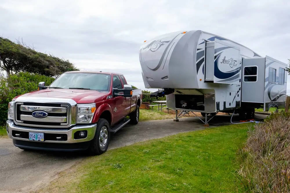 This is a large Arctic Fox fifth wheel RV with a red truck at a camp site.