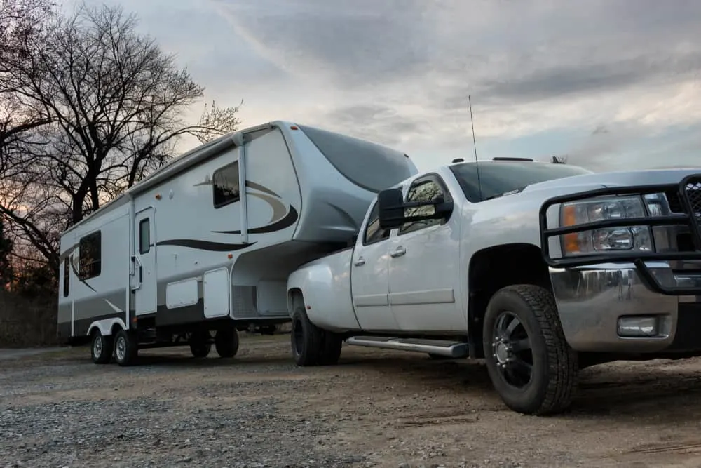 A white truck pulling a fifth wheel camper behind.