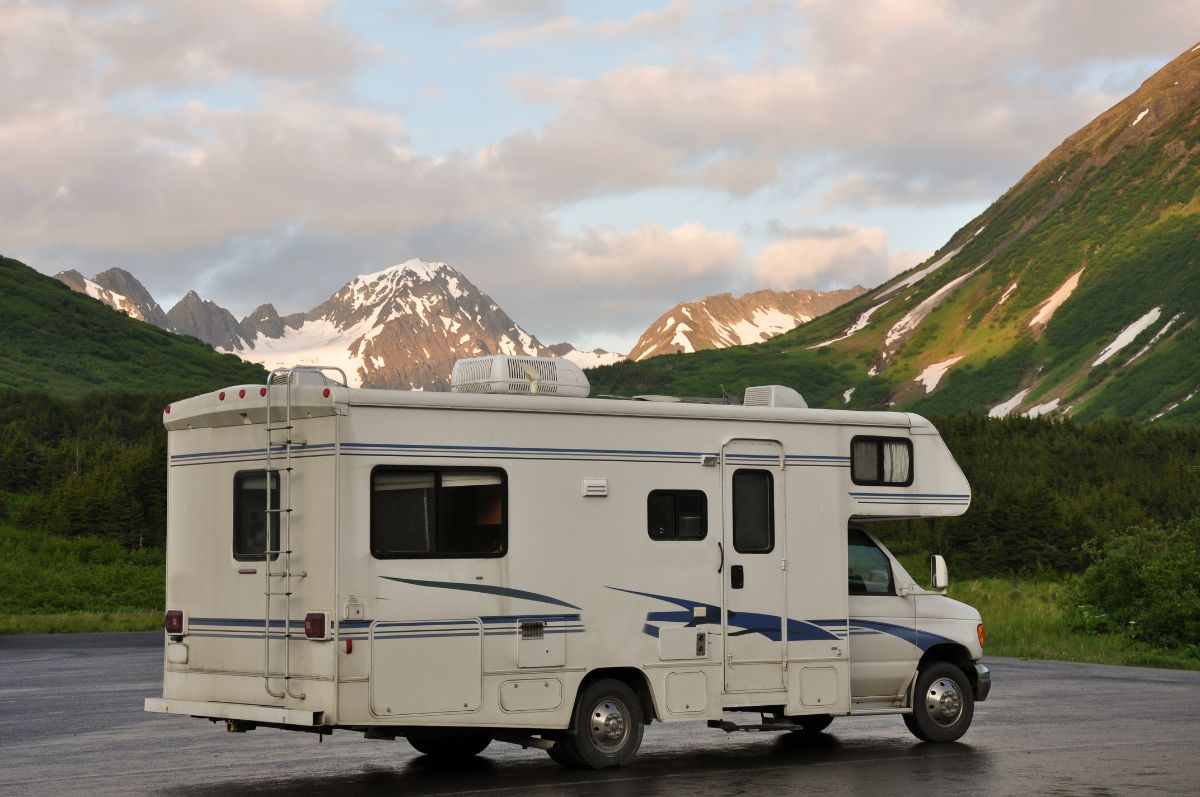 A side view of a white RV on a road near a mountain.