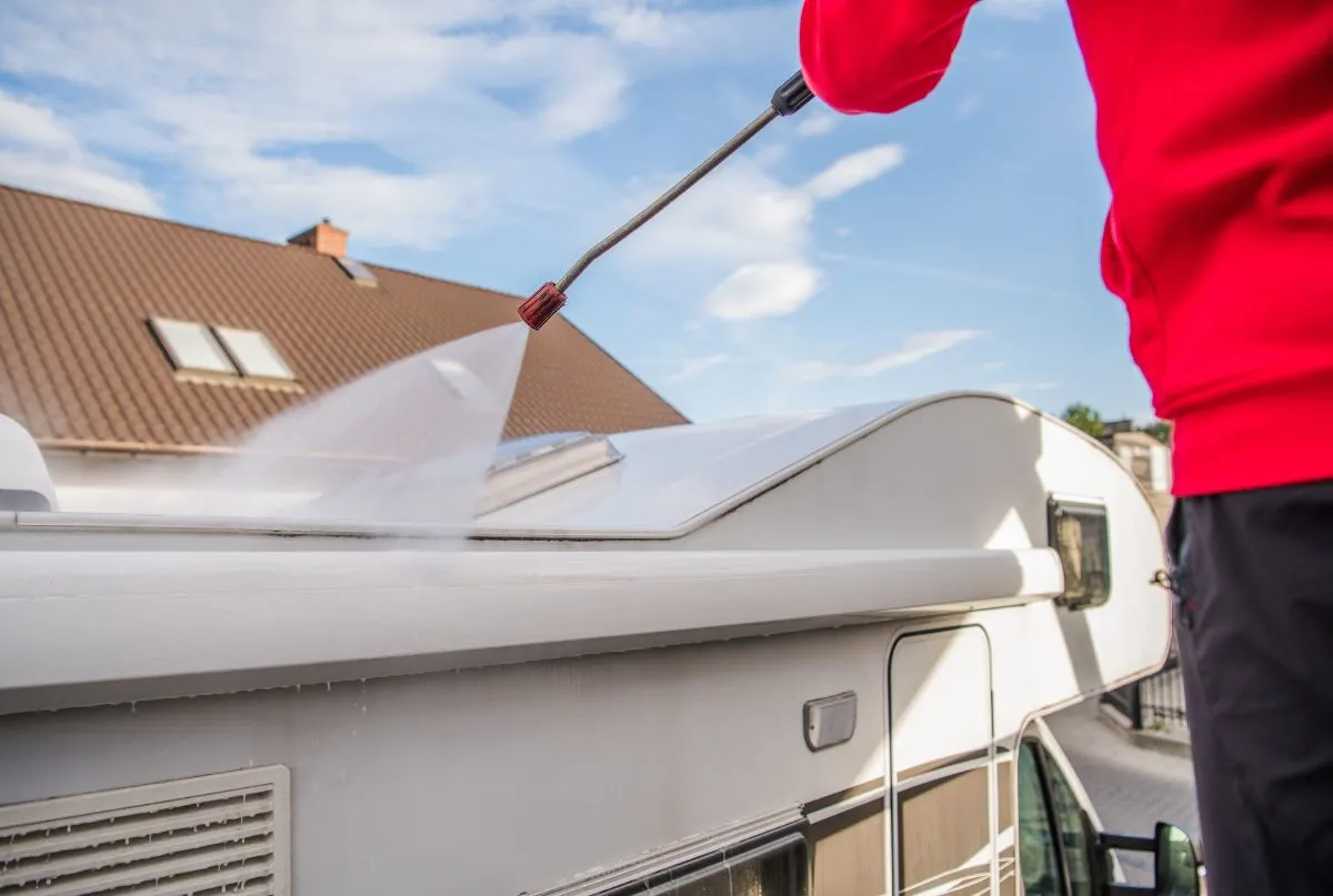 A man cleaning RV roof using water sprinkler.