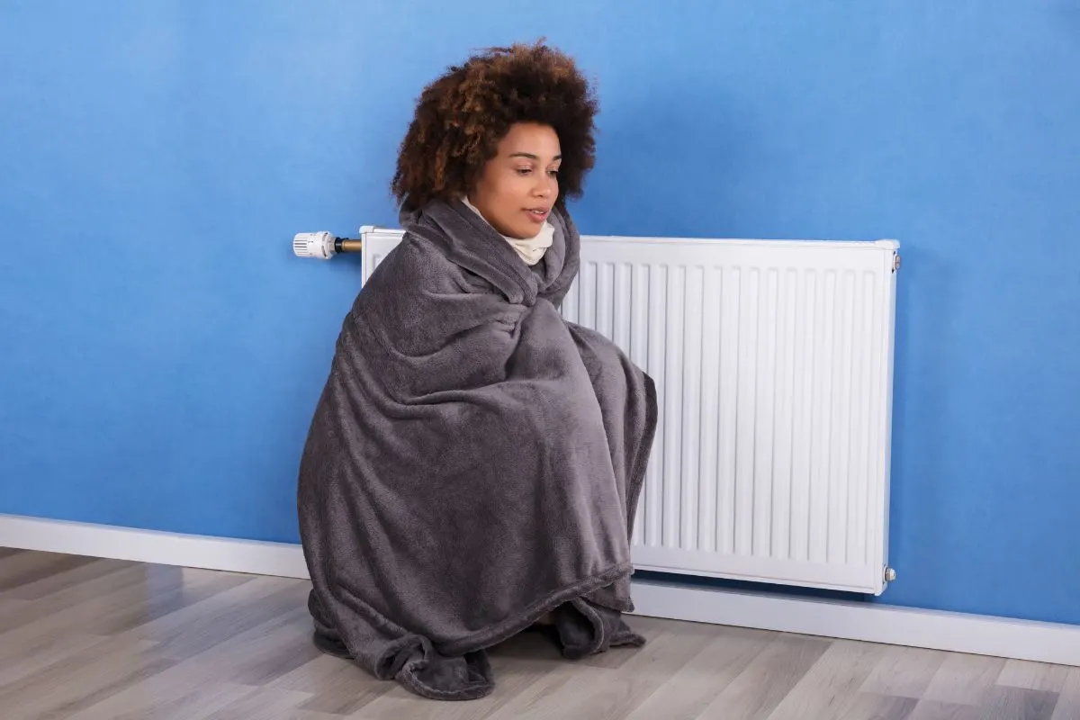 Woman wrapped up with blanket seating near a heater.