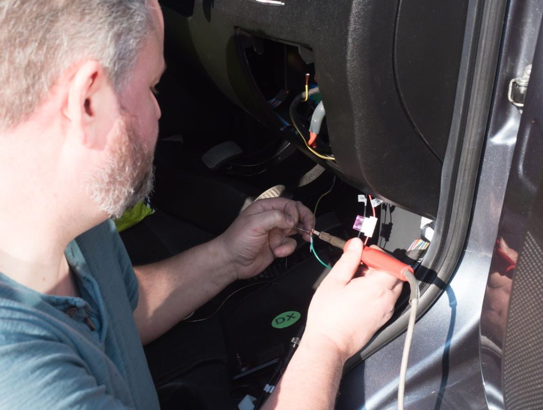 A bearded man repairing the wirings of his RV tank sensors using a soldering iron.