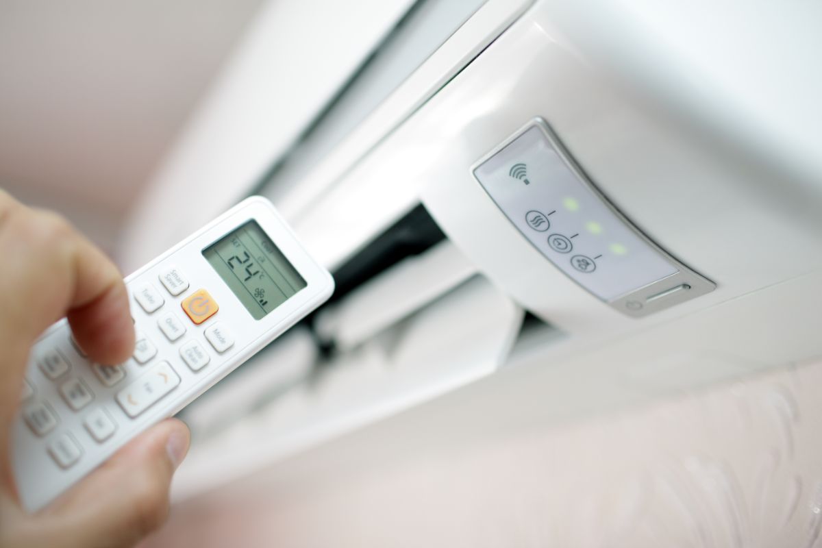 Closeup photo of air conditioner and a hand holding the remote.