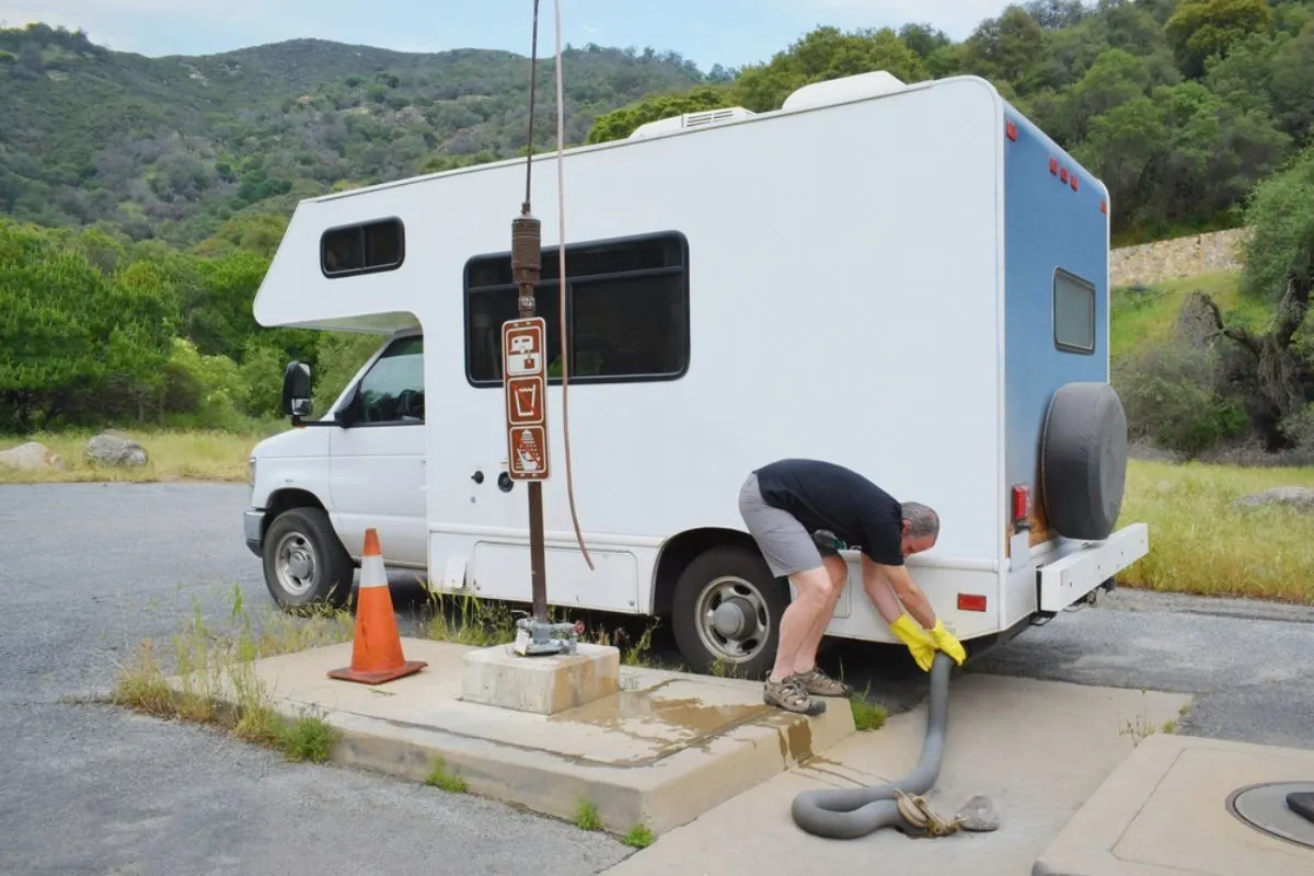 A man dumping waste water from his small RV at the dumping station.