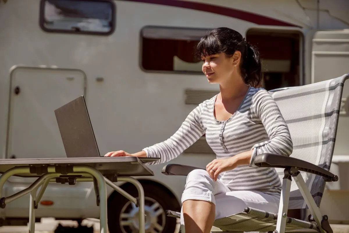 A woman seating outside an RV using a laptop.