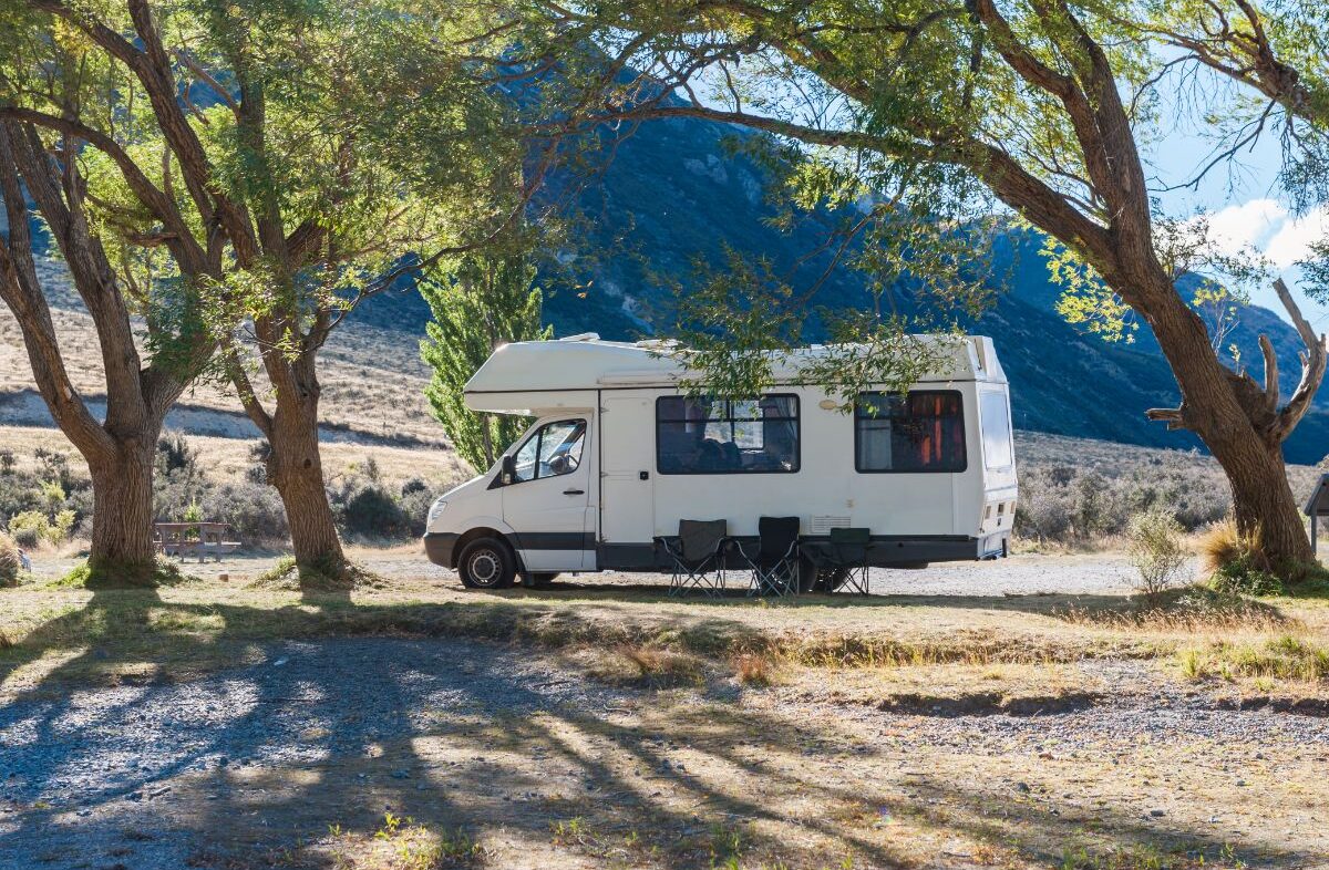 A white RV siding under the trees at the side of road.