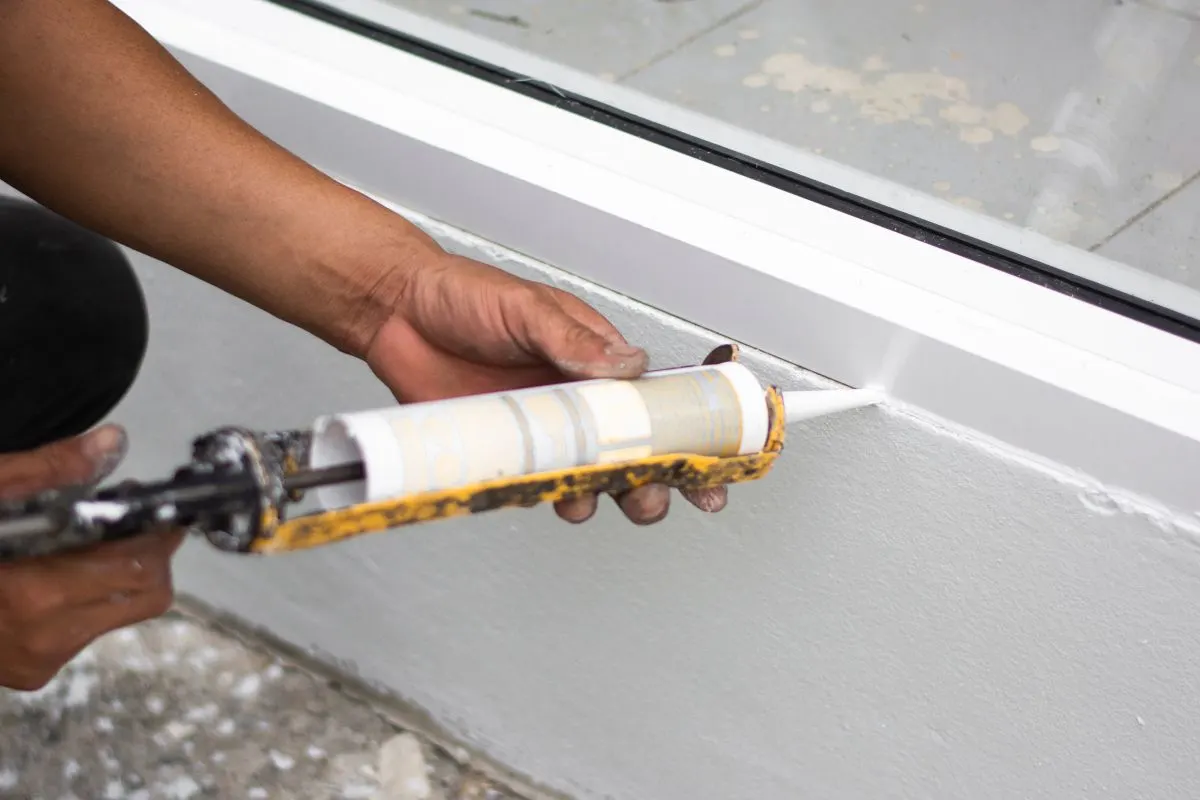 A repairman’s hand caulking holding a gun silicone.