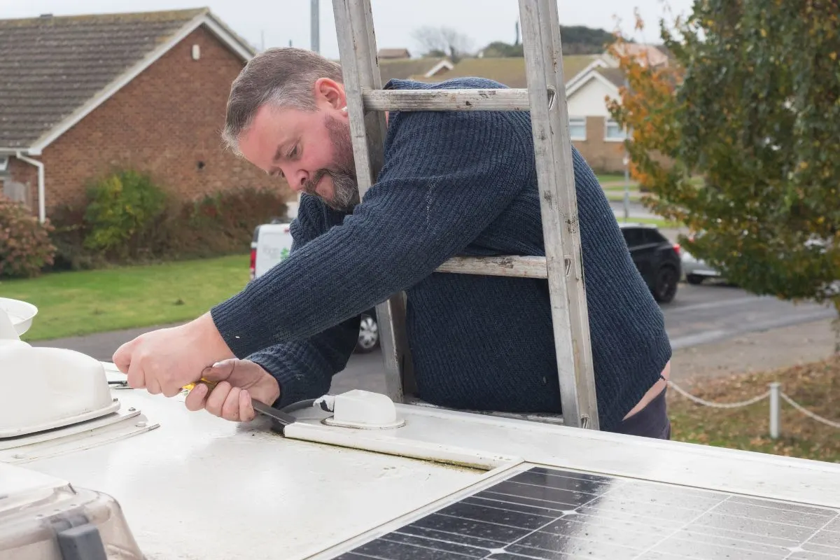 A man can be seen working from a ladder repairing the rv roof.