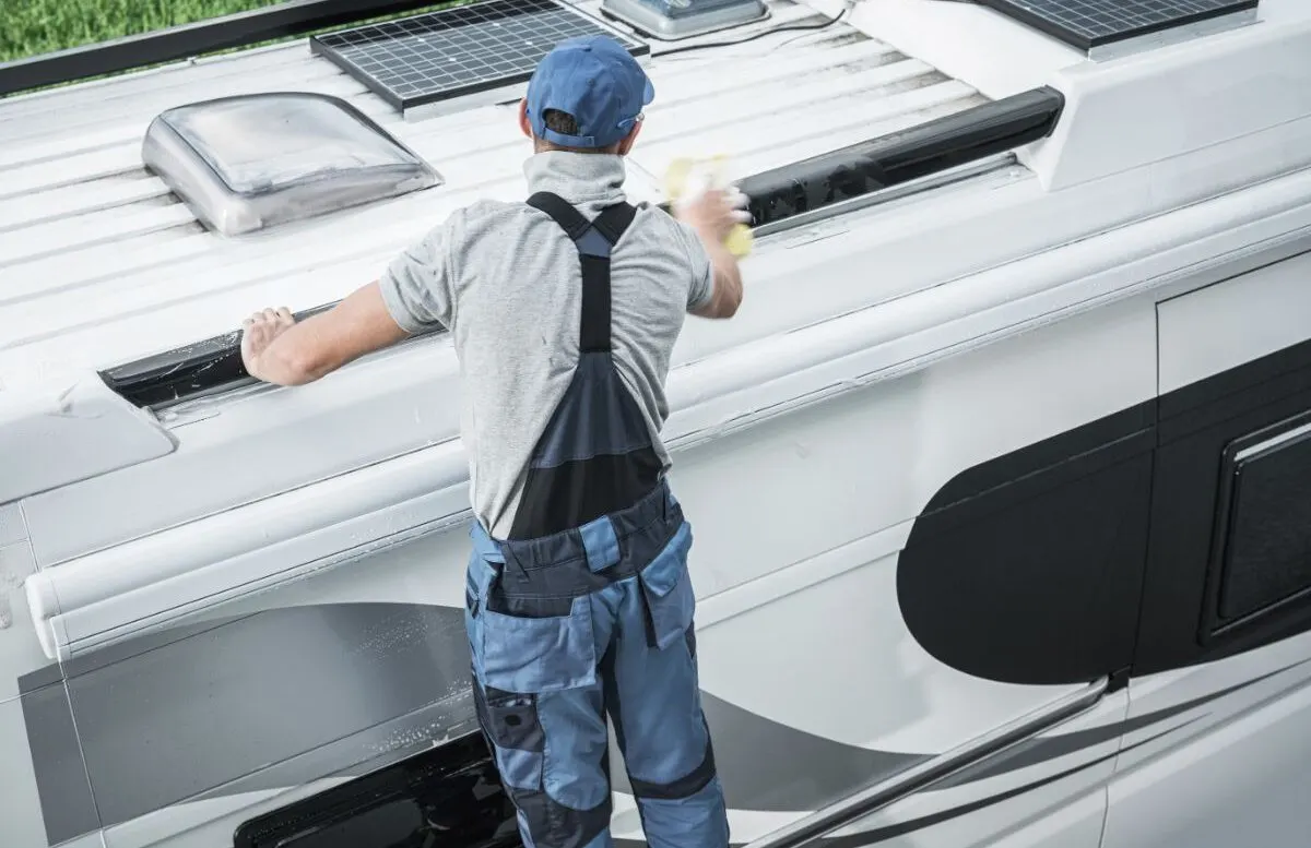 A service worker washing camper van roof using large soft sponge.