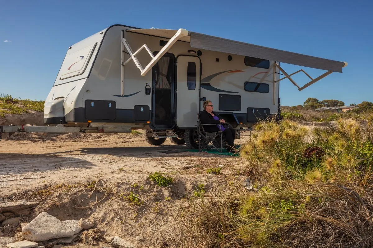 An RV with extended fixed RV awnings an an old woman seating outside.