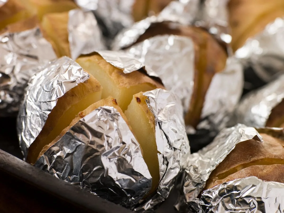 Foil wrapped potatoes on tray.