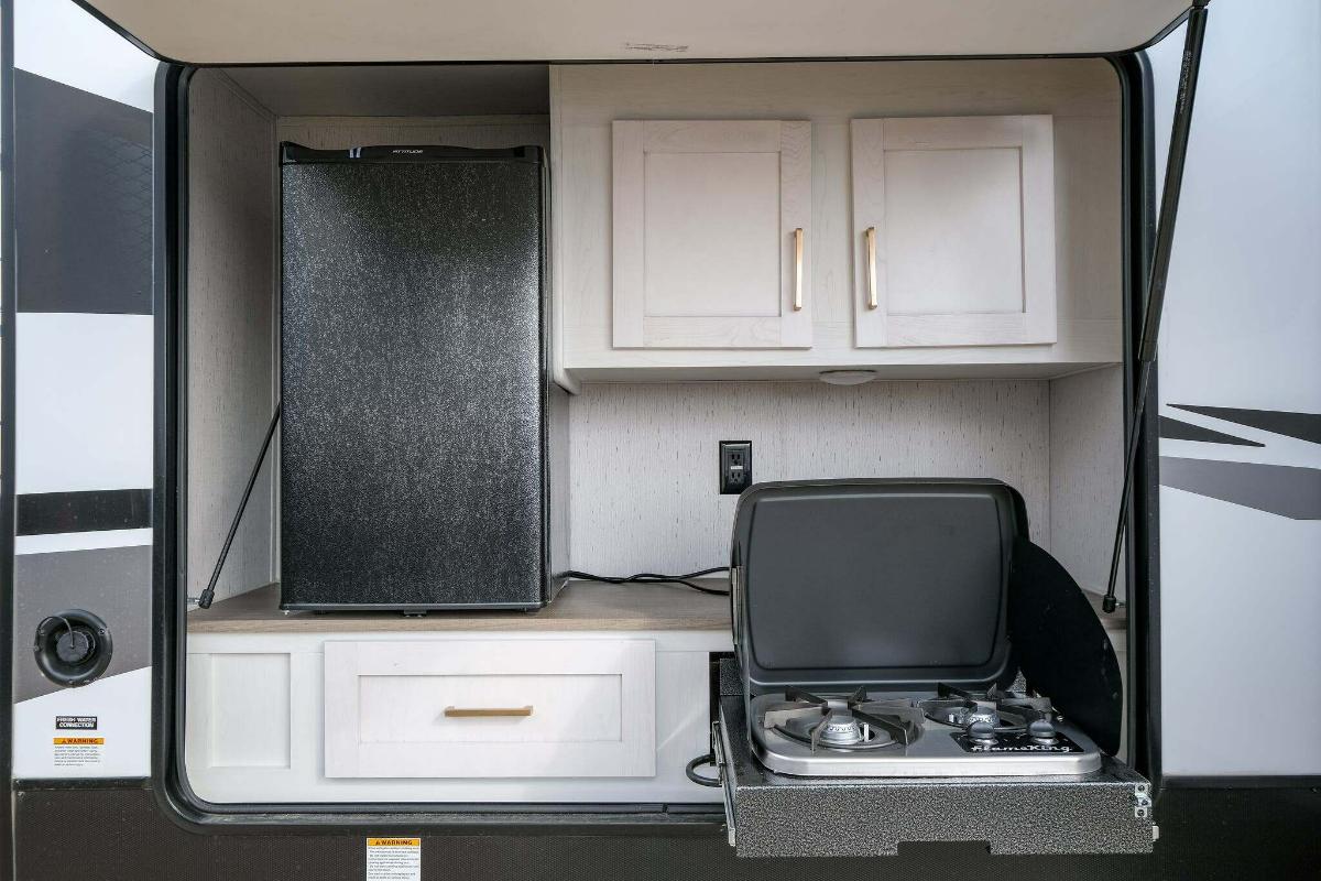 Outdoor kitchen with a gas burner, cabinets and a fridge.