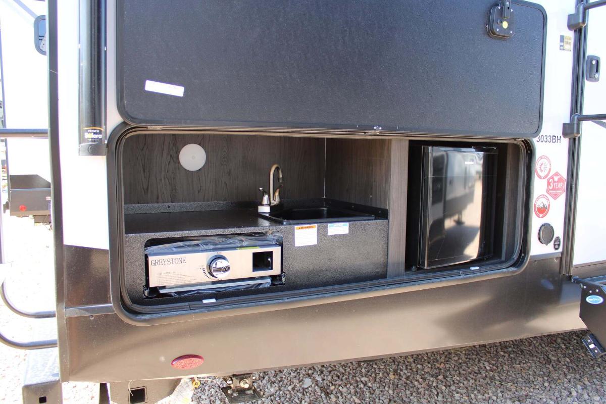 Outdoor kitchen with a gas griddle and a fridge.