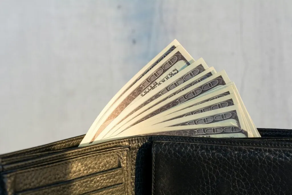 A close-up of a black leather wallet with US dollar bills sticking out.