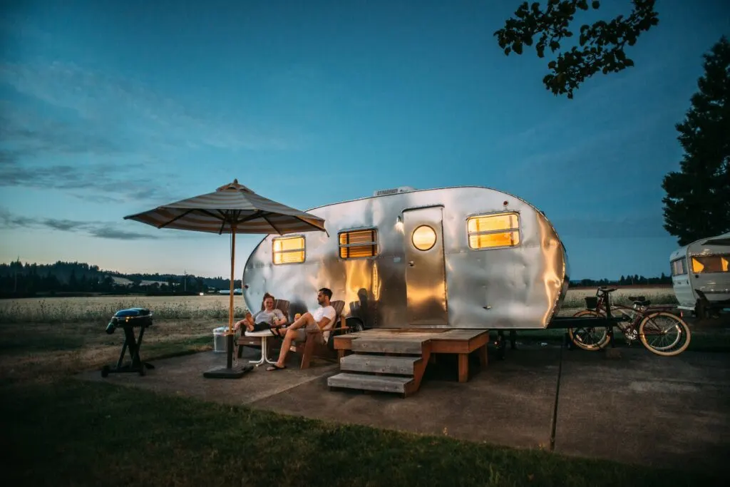 A couple is sitting on a porch of a travel trailer at night.