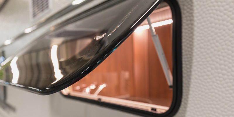 A close-up of a caravan window slightly opened to reveal a warmly lit interior, showing textural detail on the exterior.