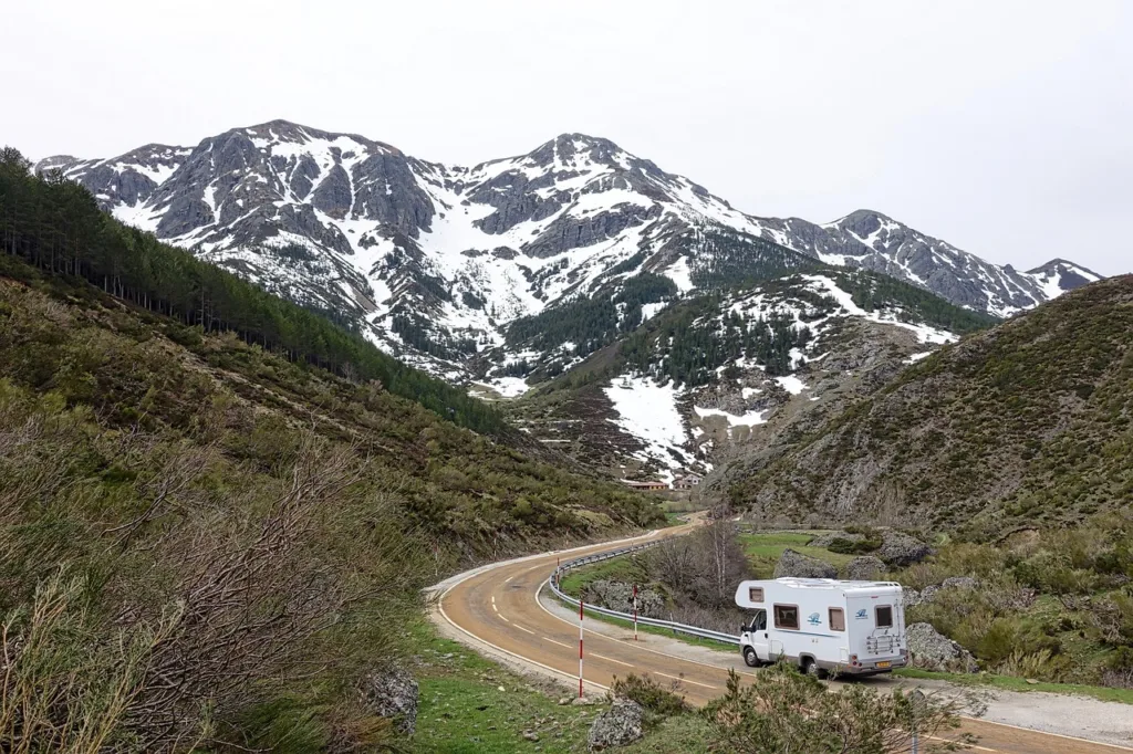 An RV traveling through a mountainous region, surrounded by snow-capped peaks and forest.