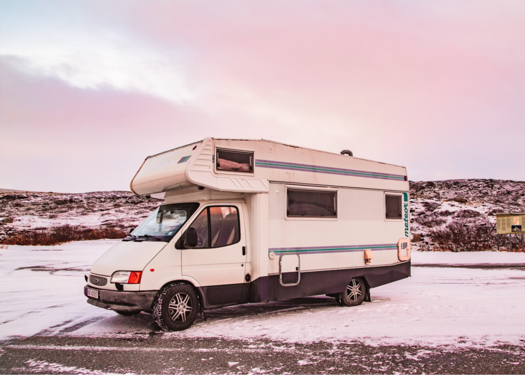 A white camper van parked on a snowy landscape with a pink sky at dawn or dusk.