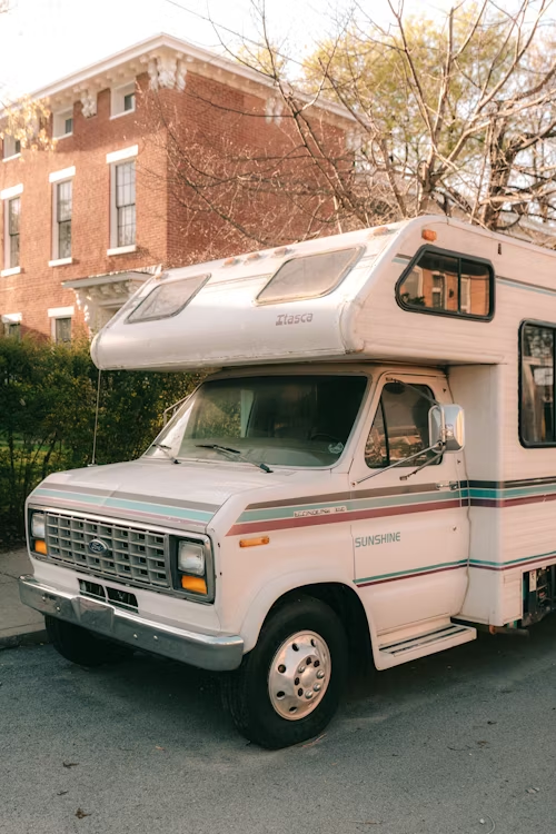 A vintage "Itasca" camper parked on a street with a brick building in the background.