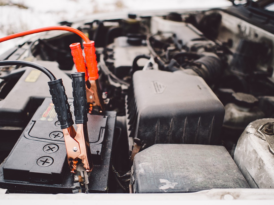 Close-up of jumper cables attached to a car battery under the hood of a vehicle.