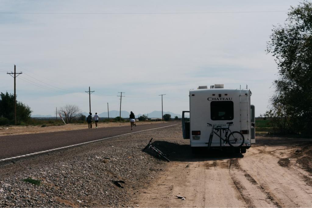 An RV parked on the side of a road with people walking or running away from it.