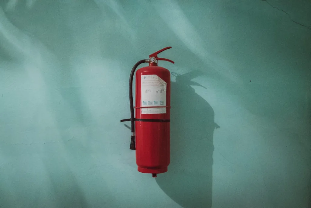 A red fire extinguisher mounted on a teal-colored wall, casting a shadow.